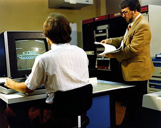 A wireframe 3D model of an M1 Abrams tank displayed on a computer screen running 1980s CAD software on a PDP11-70 computer.