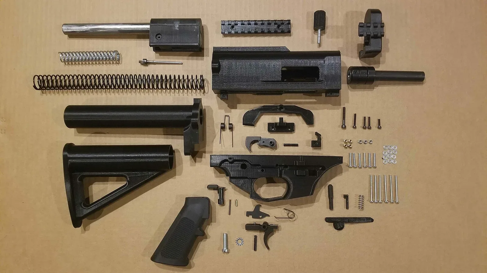 Disassembled components of the FGC-9 3D-printed firearm laid out, showing individual printed and metal parts.