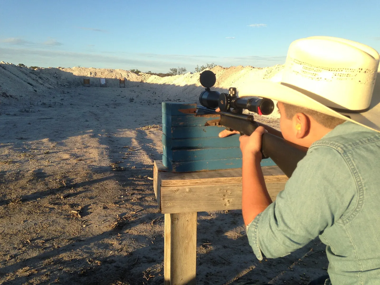 A man at a shooting range aiming a rifle at a target in preparation for hunting season.