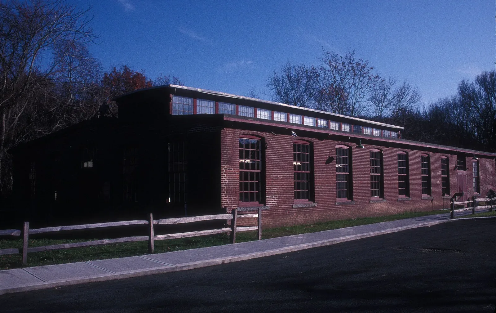 Historical photograph of Eli Whitney's gun factory, a multi-story brick industrial building with regular window patterns, representing early American manufacturing infrastructure