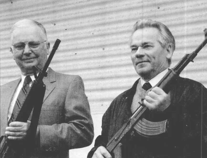 Eugene M. Stoner on the left and Mikhail T. Kalashnikov on the right, both holding their respective assault rifles