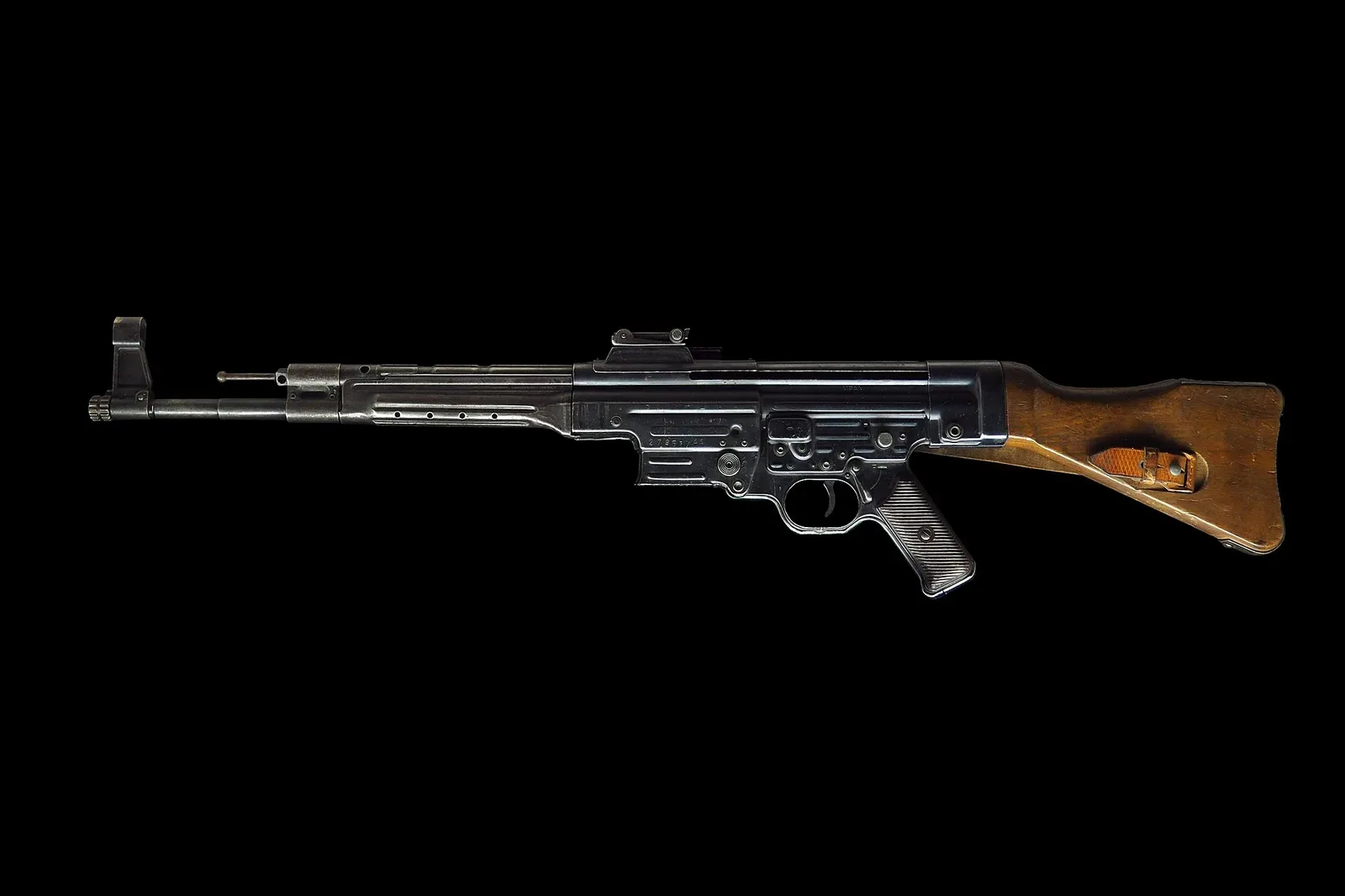 Detail view of a Sturmgewehr 44 assault rifle displayed against a black background, showing the weapon's distinctive profile with curved magazine, wooden furniture, and gas tube system.
