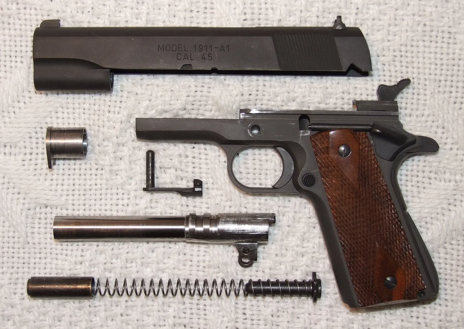 Side profile view of a 1911A1 pistol displayed against a neutral background, showing the full length of the slide, frame, grip, and trigger guard