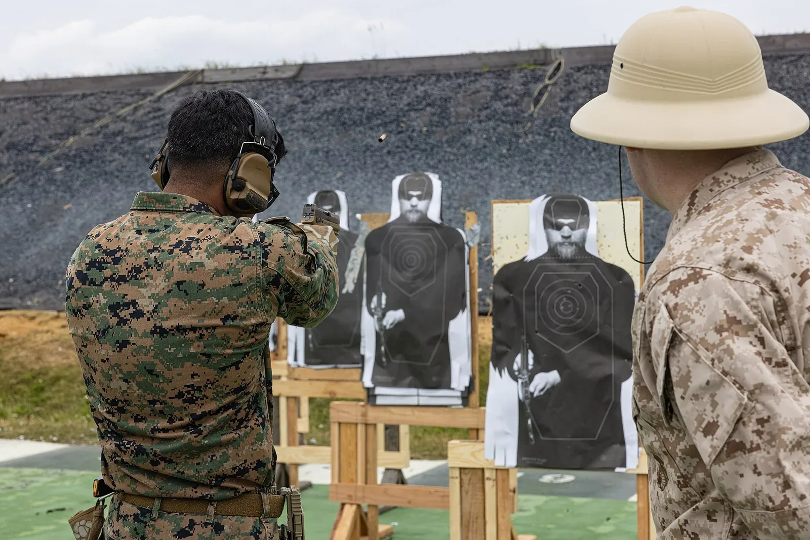 Marine shooters in prone position aiming pistols at targets during a competitive shooting practice session