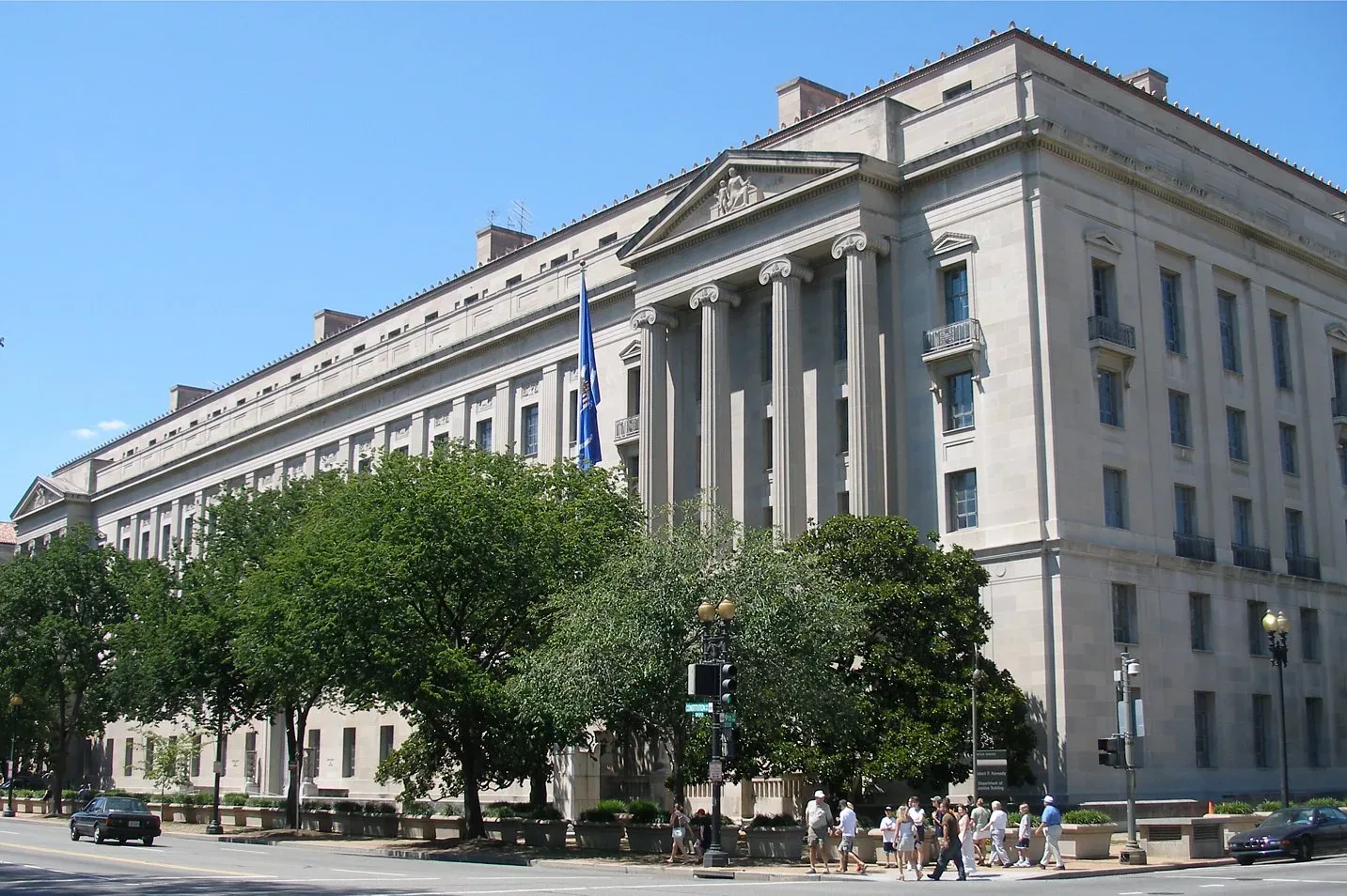The exterior of the United States Department of Justice headquarters building in Washington, D.C., a neoclassical stone structure photographed during daytime.