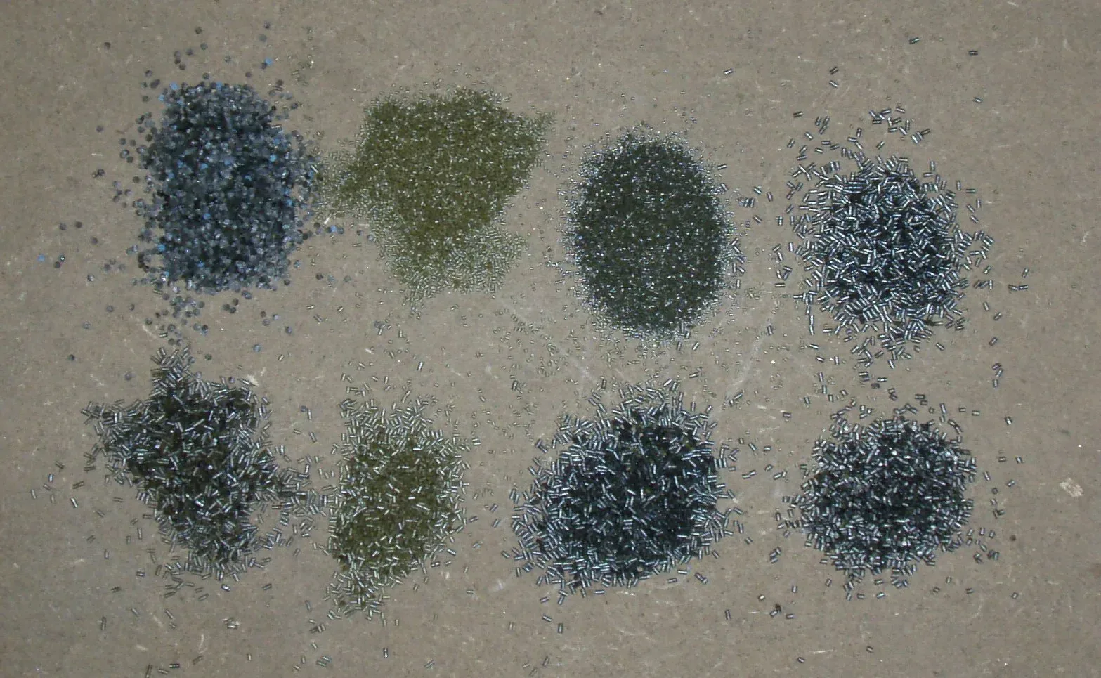 Five different smokeless powder samples arranged in a row, showing visual variations in granule size, shape, and color ranging from fine spherical particles to larger irregular flakes.