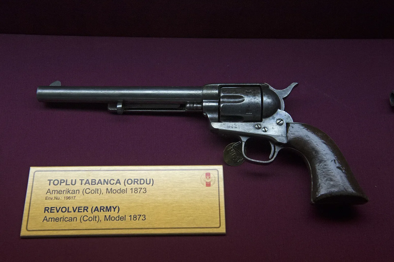 Colt 1873 single-action revolver displayed in a museum case, showing the full profile and mechanical details of the iconic cowboy revolver
