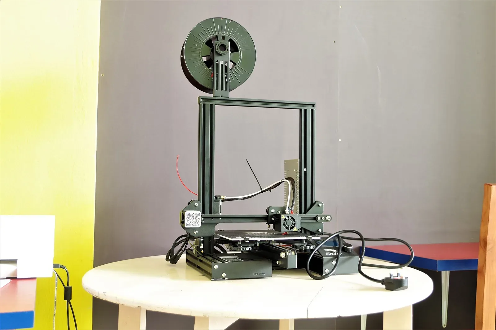 A desktop 3D printer with white frame and heated build platform, shown from an angled front view in a laboratory or maker space setting.