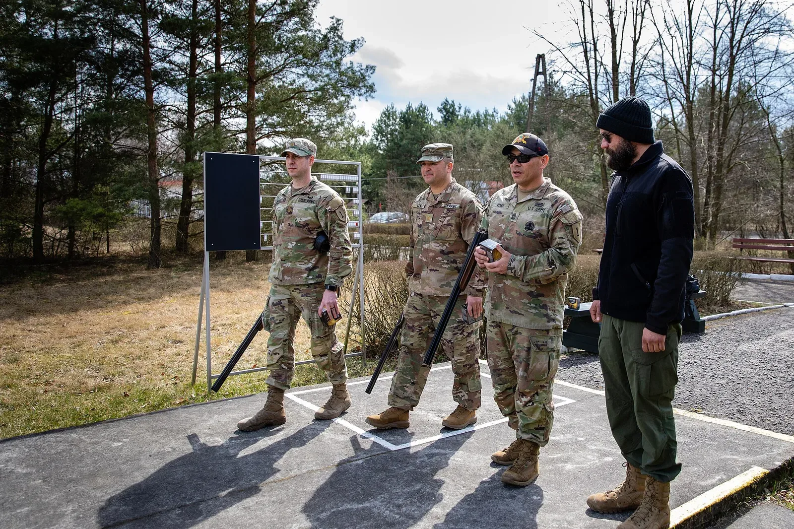 A clay target shooter wearing safety glasses and hearing protection while at an outdoor shooting range, demonstrating proper safety equipment usage.