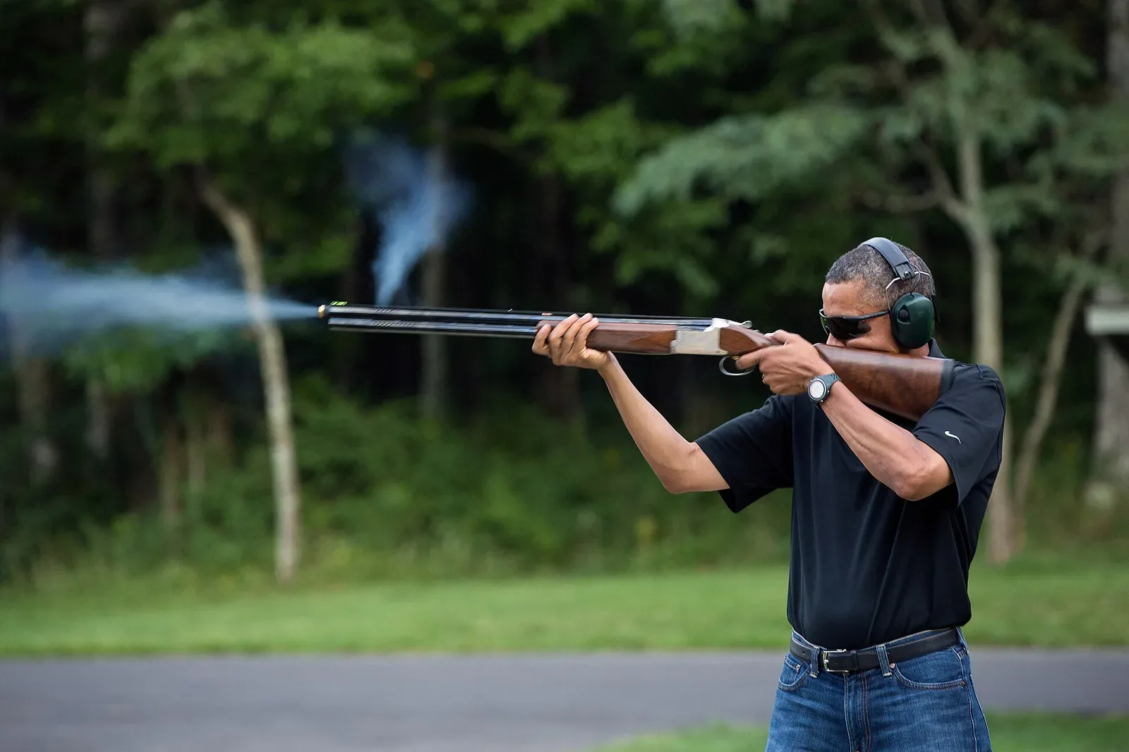 A person in shooting stance aiming a shotgun at clay targets during a shooting sport activity
