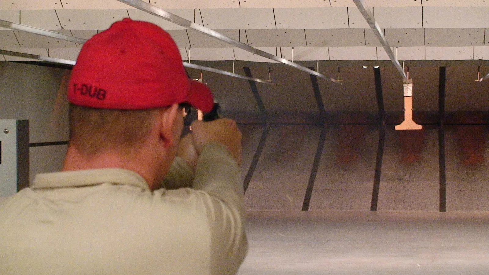 Person at an indoor firing range demonstrating handgun shooting technique with proper stance and finger placement
