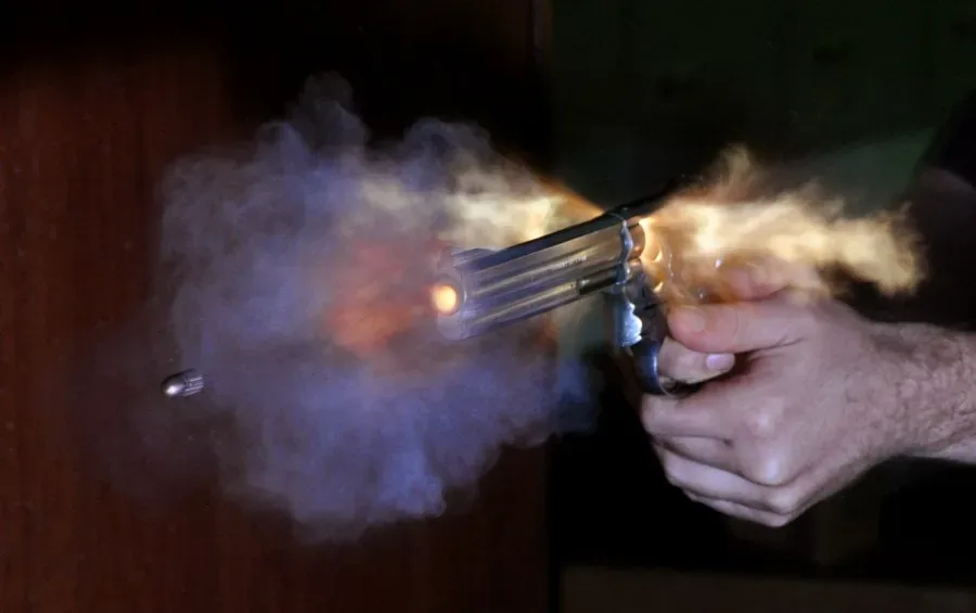 Ultra-high-speed photograph of a bullet exiting the muzzle of a Smith & Wesson revolver, showing the projectile in flight with visible shock waves or vapor clouds around it.