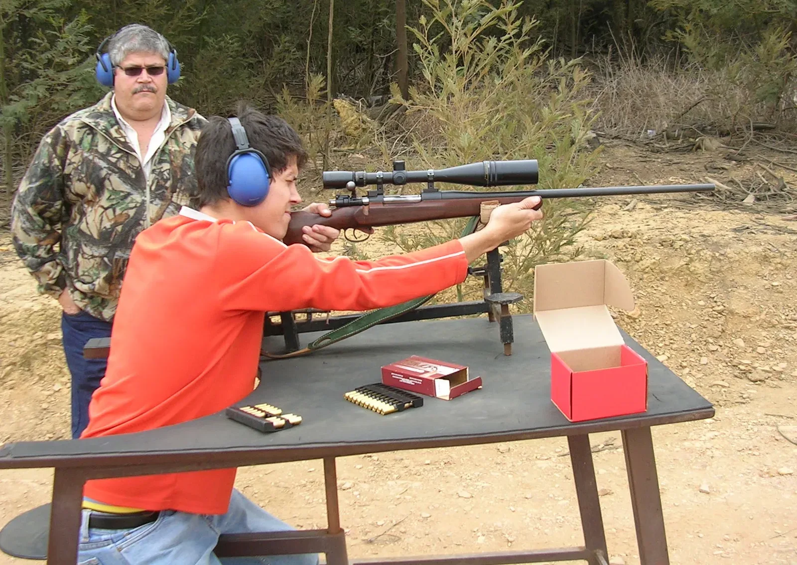 A youth shooter at a shooting bench, aiming a Mauser hunting rifle with proper form and stance.