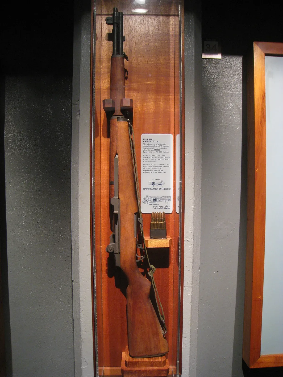M1 Garand rifle displayed at the US Army Museum of Hawaii, shown in full profile against a neutral background, displaying the complete rifle with wood furniture and metal components