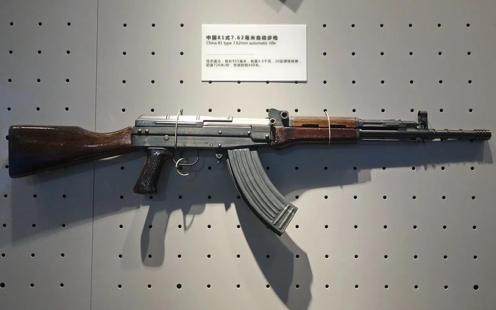 Type 81 assault rifle displayed against a neutral background, showing the complete rifle profile with gas tube above the barrel and wooden furniture.