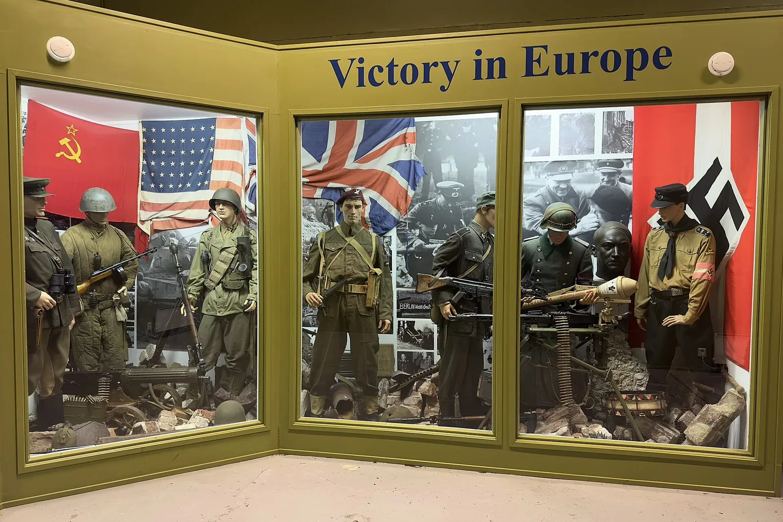 Museum display of World War II weapons and uniforms from multiple nations including Soviet, American, British, and German forces, showing submachine guns and military equipment from the Allied and Axis powers.