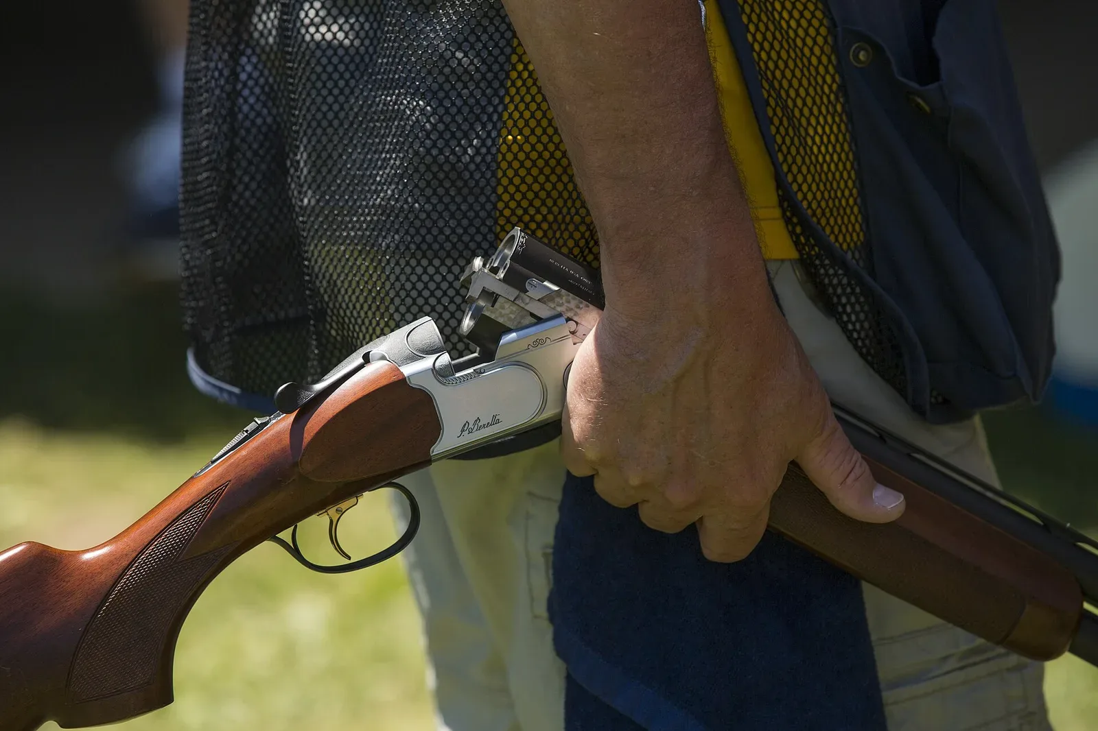 A trap shooter in competition stance aiming a shotgun at clay targets during a shooting event.