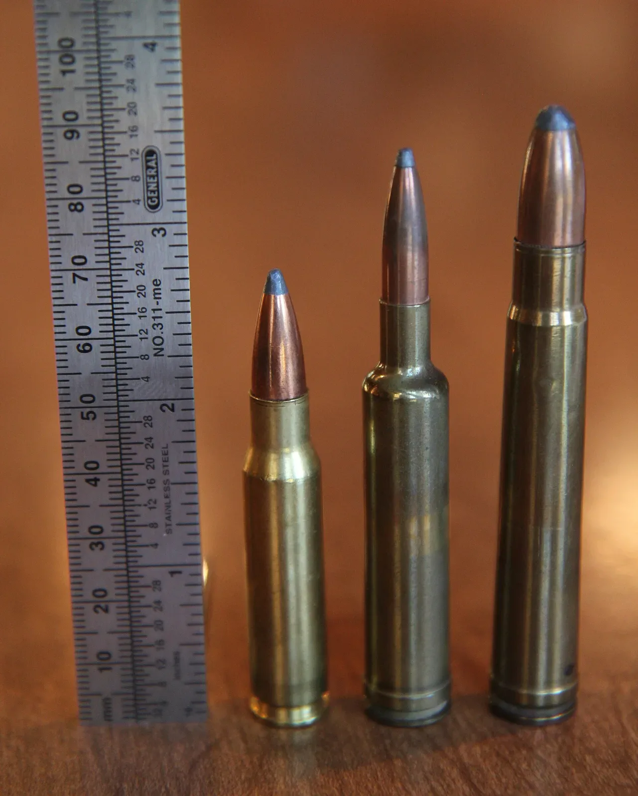Three rifle cartridges arranged next to a ruler: .257 Weatherby Magnum in the center, .308 Winchester, and .375 H&H Magnum, showing relative size comparison.