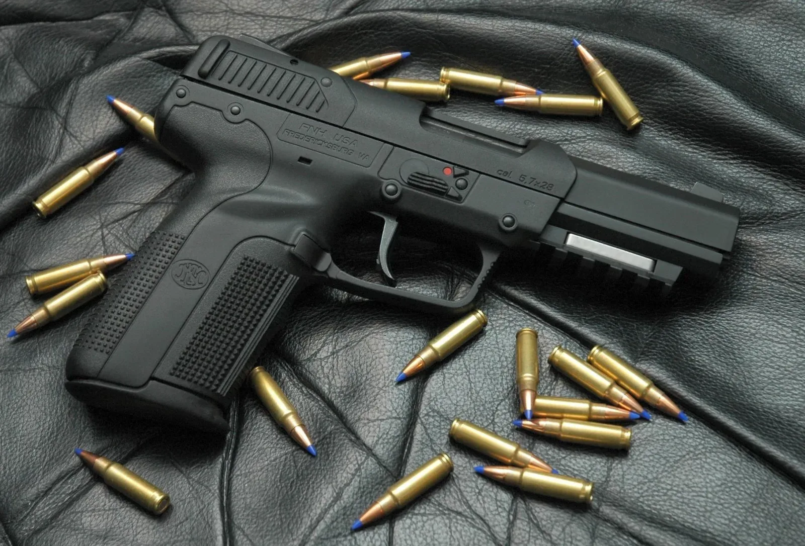 FN Five-seveN USG pistol in black finish displayed with approximately twenty FN 5.7×28mm cartridges arranged around it