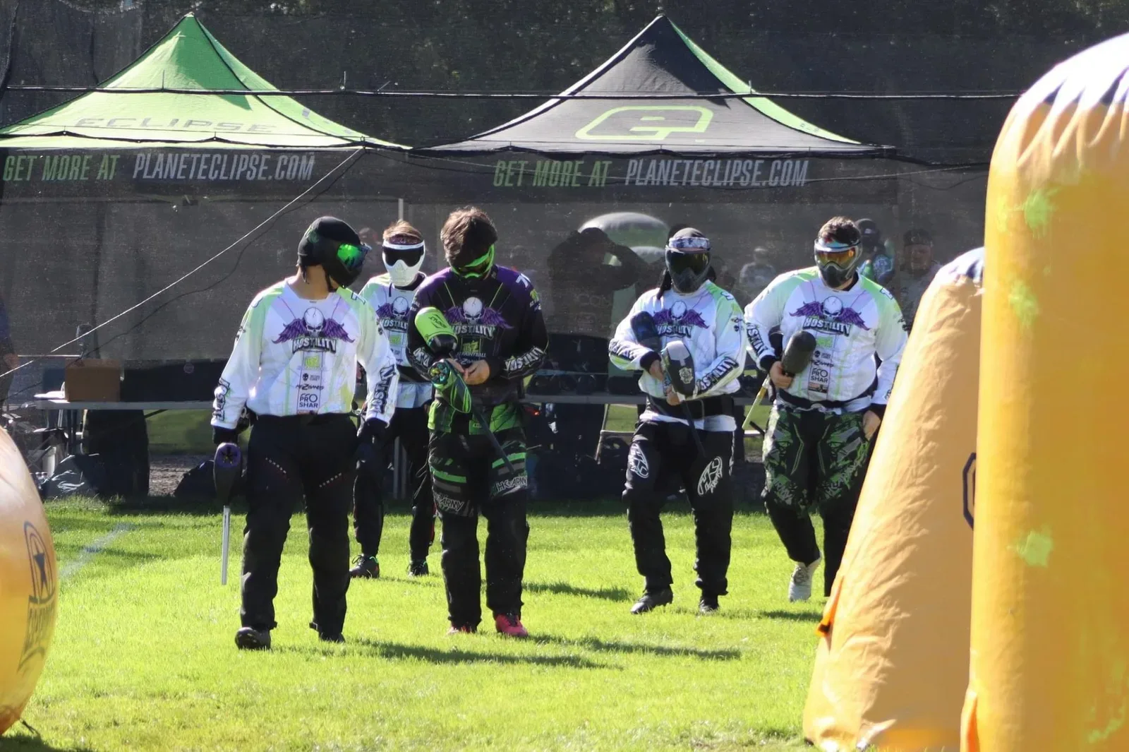 A competitive paintball team positioned on a sup-air field with inflatable bunkers during tournament play, players in tactical gear with markers ready.