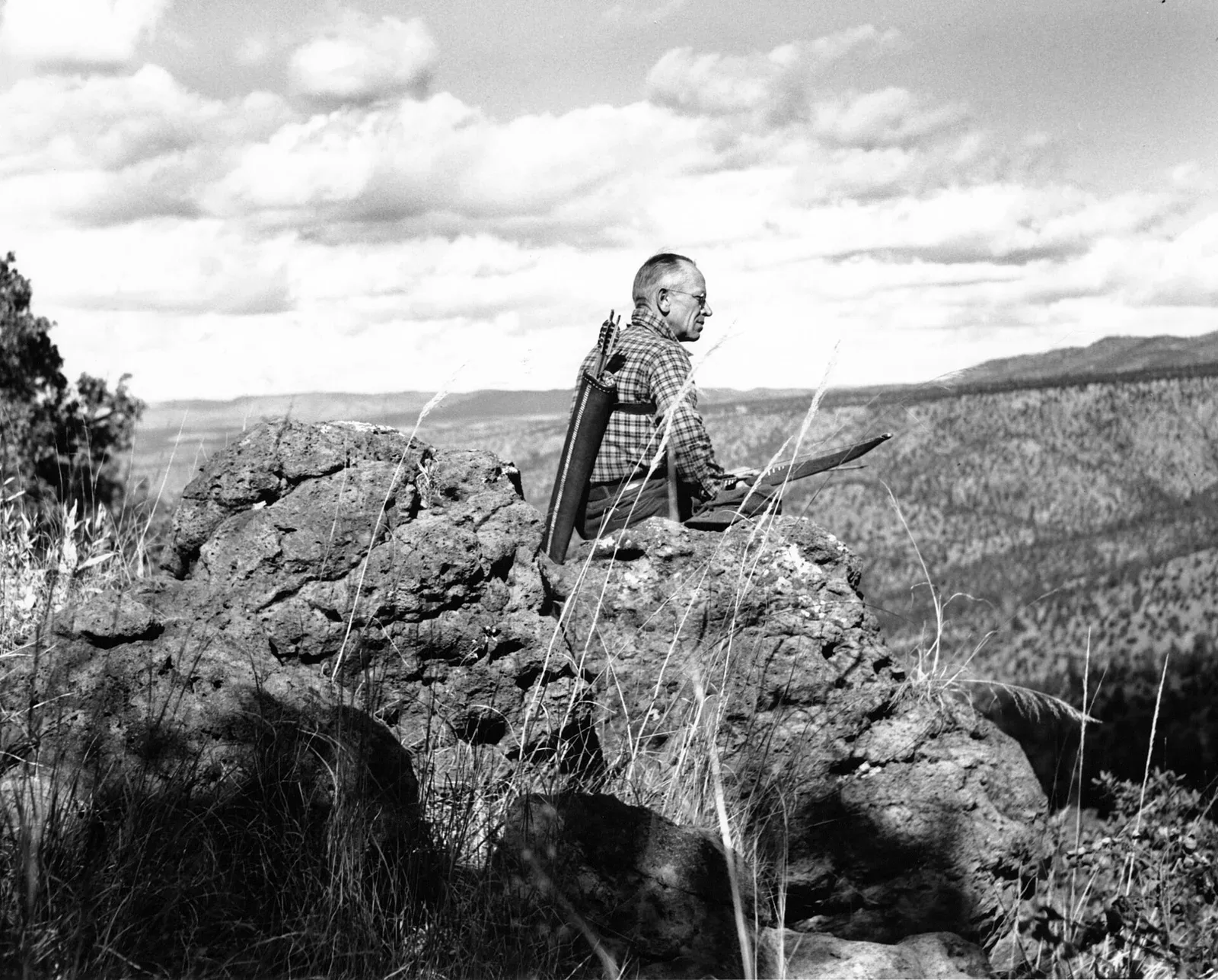 Aldo Leopold seated on rimrock overlooking the Rio Gavilan in northern Mexico, holding a bow and quiver