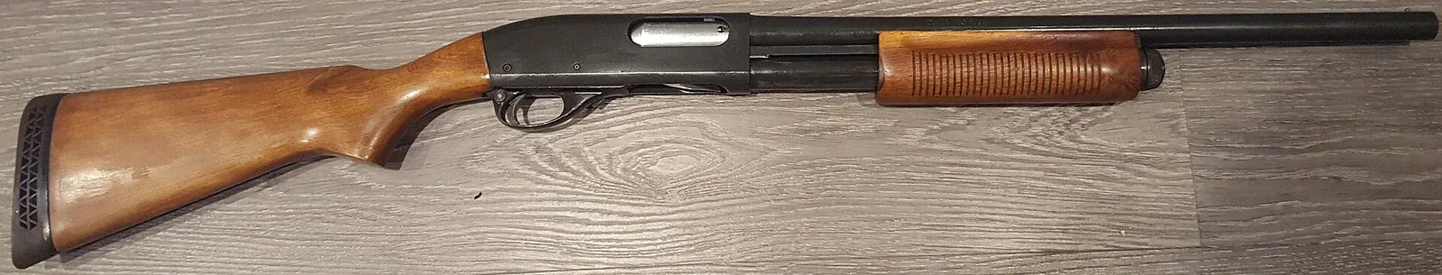 Disassembled Remington 870 Wingmaster shotgun showing the receiver, barrel, foregrip with dual steel action bars, bolt assembly, and internal operating components laid out horizontally.