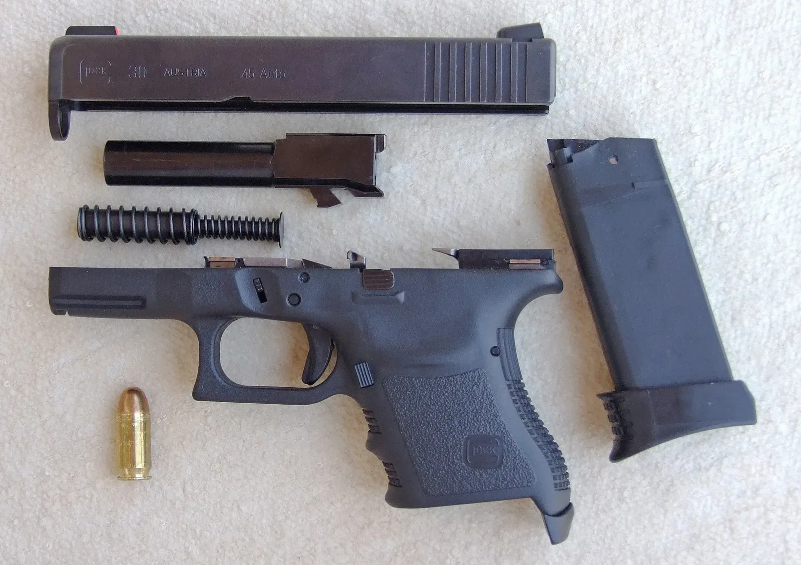 A Glock 30 subcompact pistol field stripped into its main component parts, displayed with a single 45 ACP cartridge for scale