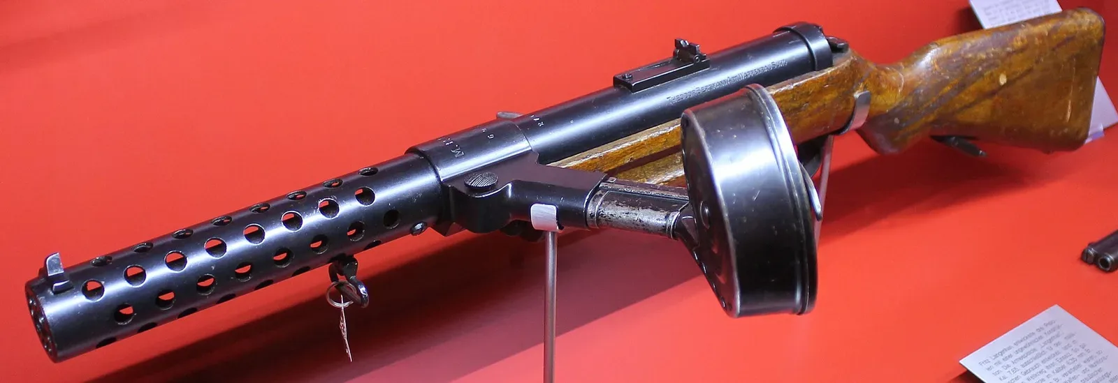 Side view of an MP18 submachine gun displayed against a neutral background, showing the distinctive profile and mechanical details of the first modern submachine gun.