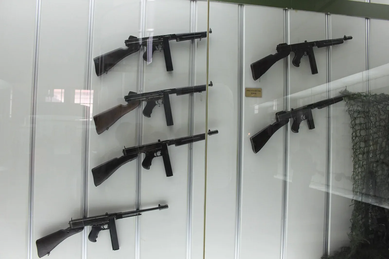 Thompson submachine gun displayed against a neutral background, showing the full profile of the weapon with its distinctive drum magazine and horizontal foregrip