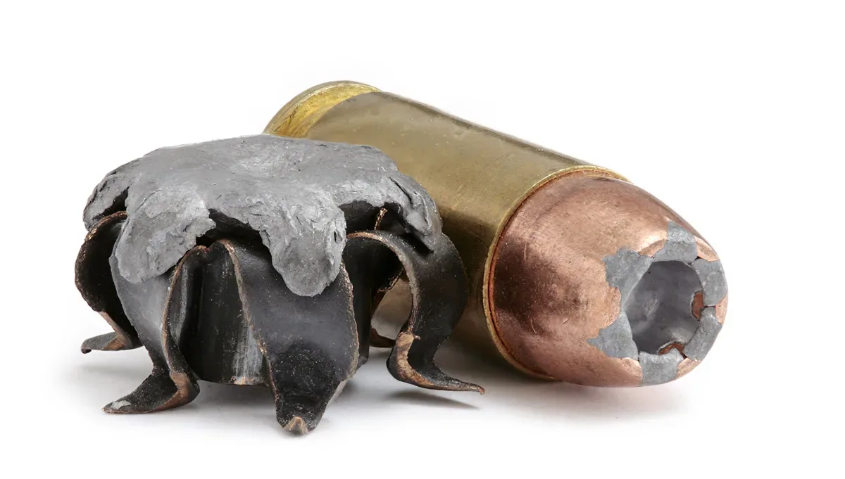 A .40 S&W cartridge positioned next to an expanded hollow point bullet, showing the mushroom-shaped deformation characteristic of hollow point ammunition after firing.