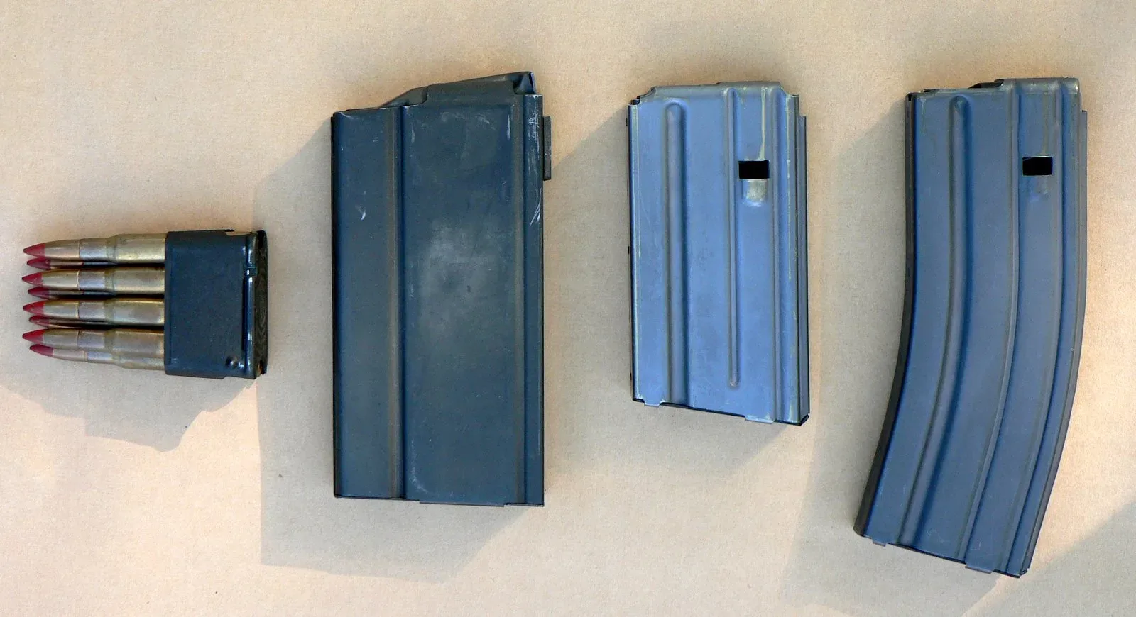 Three military magazines displayed side by side: an 8-round M1 Garand clip, a 20-round M14 magazine, and 20-round and 30-round AR-15/M16 magazines.