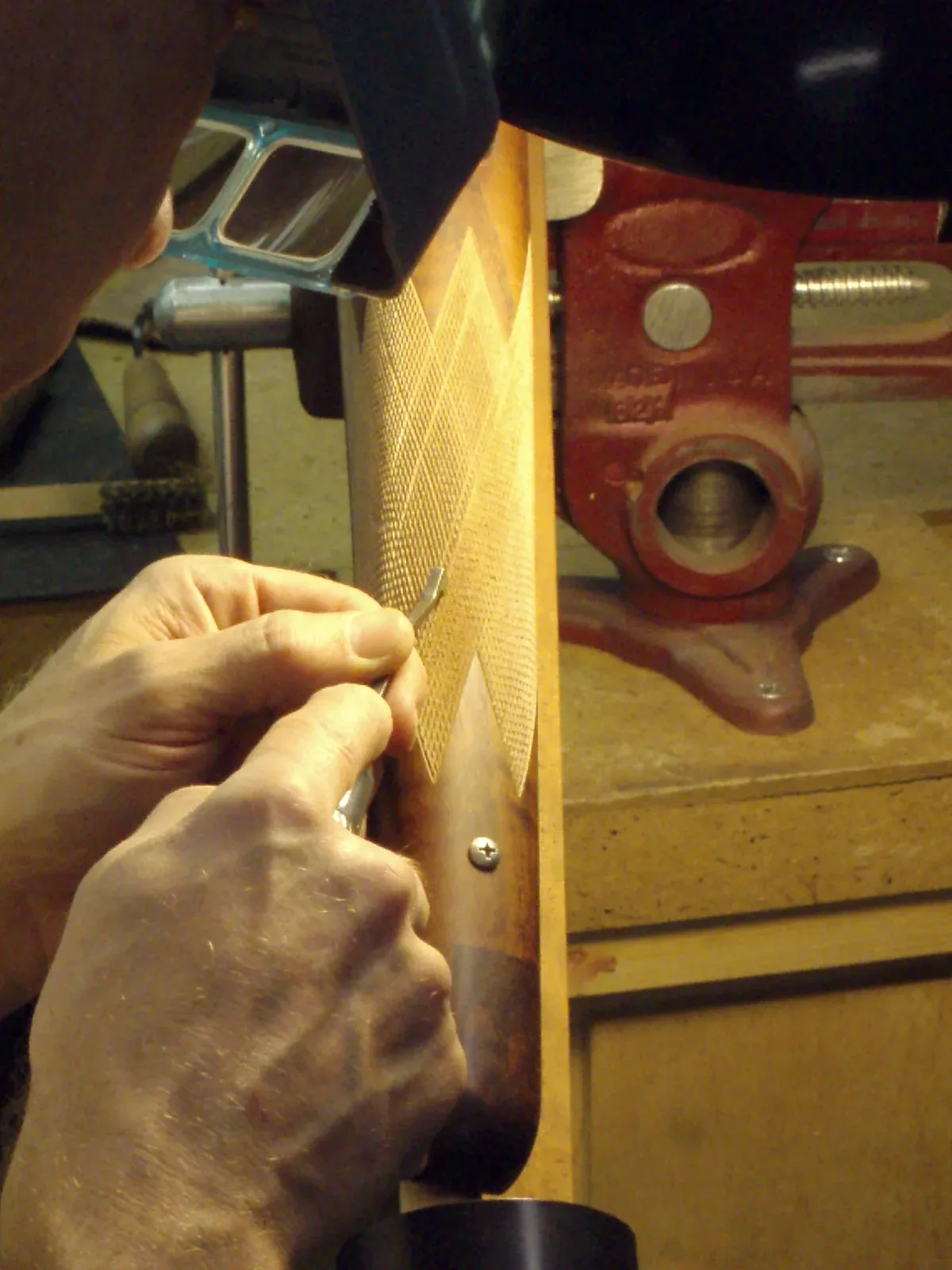 A gunsmith performing checkering work on a rifle stock using hand tools and a checkering file.